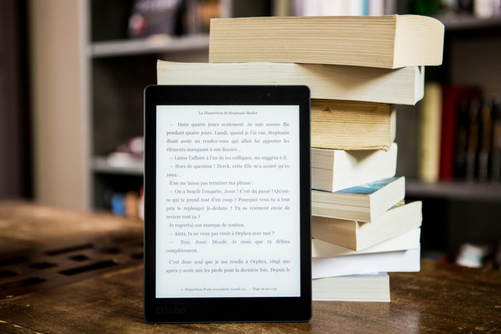 Hvilket bogformat passer til din hverdag? E-reader with text displayed next to a stack of physical books on a wooden table.